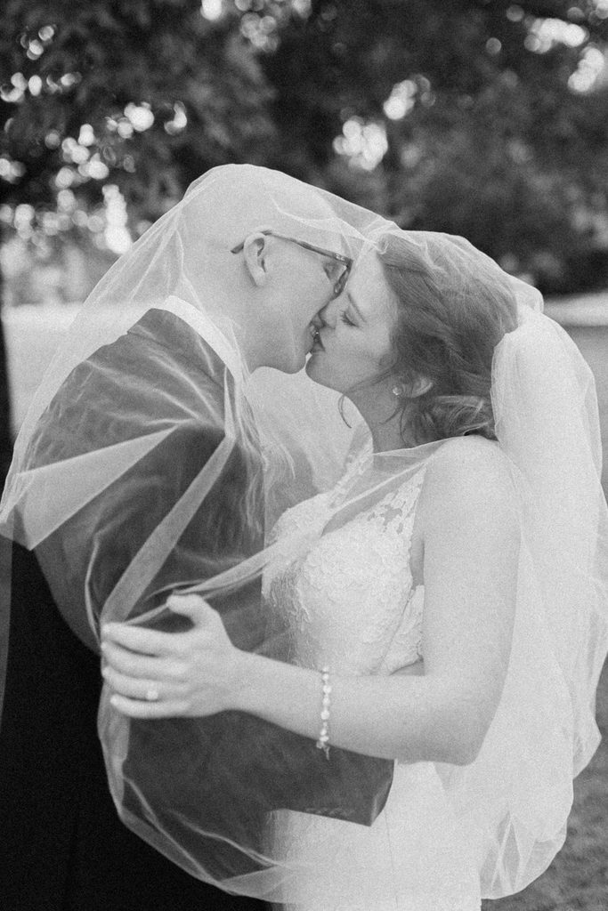 Bride and groom kissing under the bride's veil in a black and white cropped close up shot.