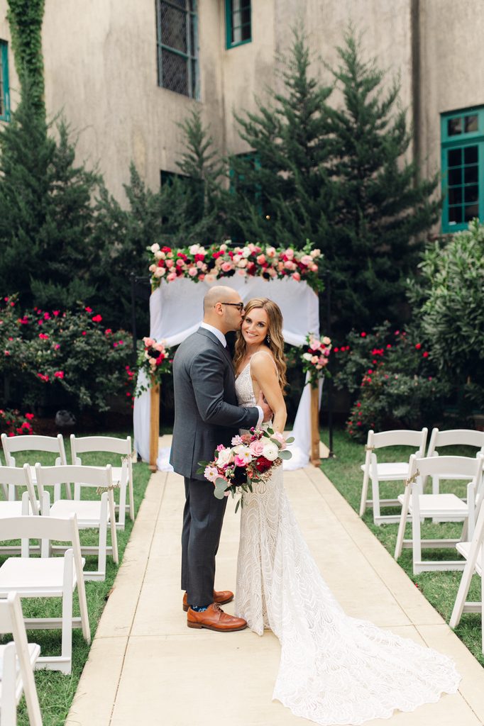 Bride and groom posing where their ceremony takes place at dresser mansion in tulsa. The groom is kissing the bride's temple while the bride is smiling at the camera