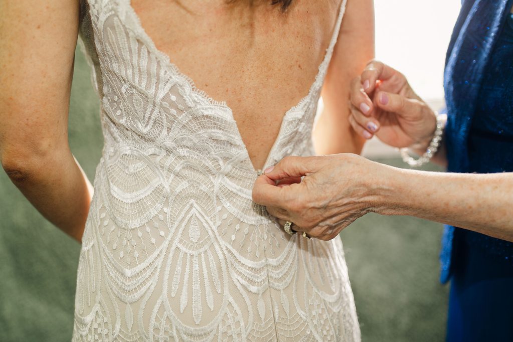 Close-up of Megan’s lace wedding gown being fastened during bridal preparations. 