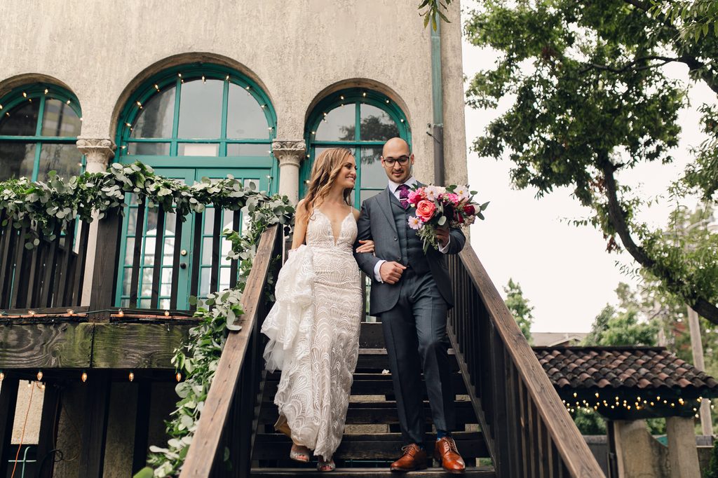 Megan and Keivan walking arm in arm down outdoor wooden steps decorated with greenery at Dresser Mansion. 