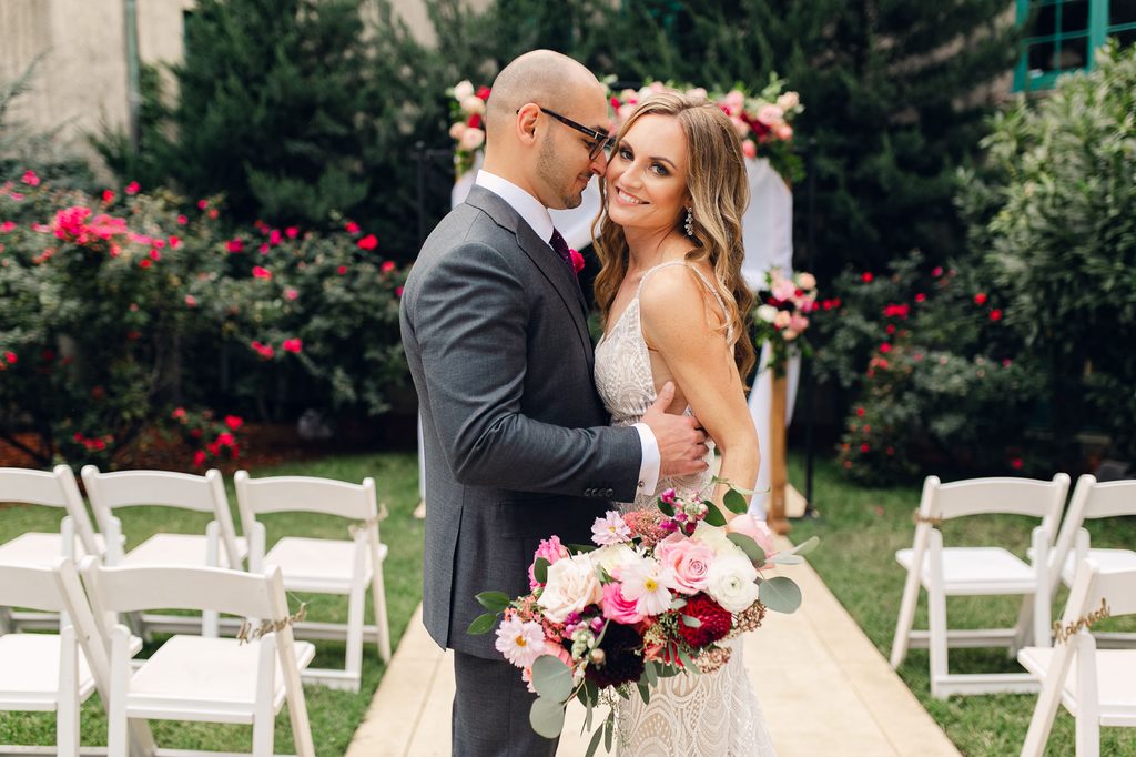 Keivan facing Megan in the outdoor wedding aisle, with a floral ceremony backdrop behind them.