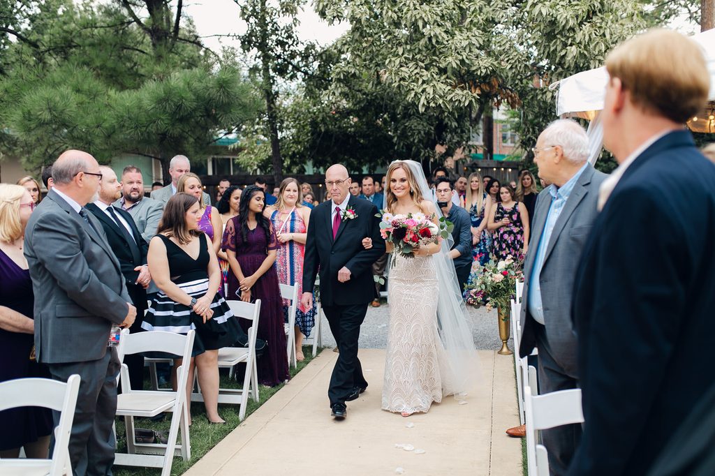 Megan walking arm in arm with her father down the wedding aisle, carrying her colorful bouquet. 