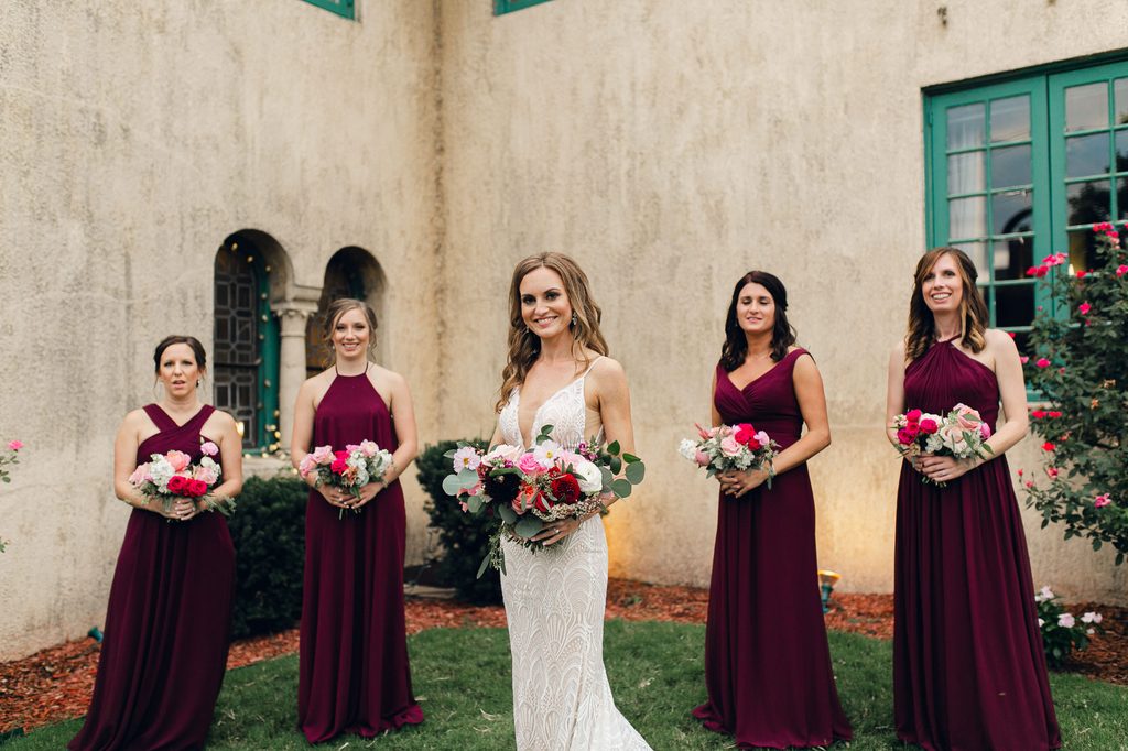 Megan and four bridesmaids in floor-length burgundy dresses holding colorful bouquets outside Dresser Mansion. 
