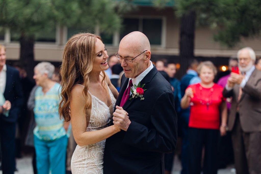 Megan smiling toward her father during their father-daughter dance, with guests gathered around them. 