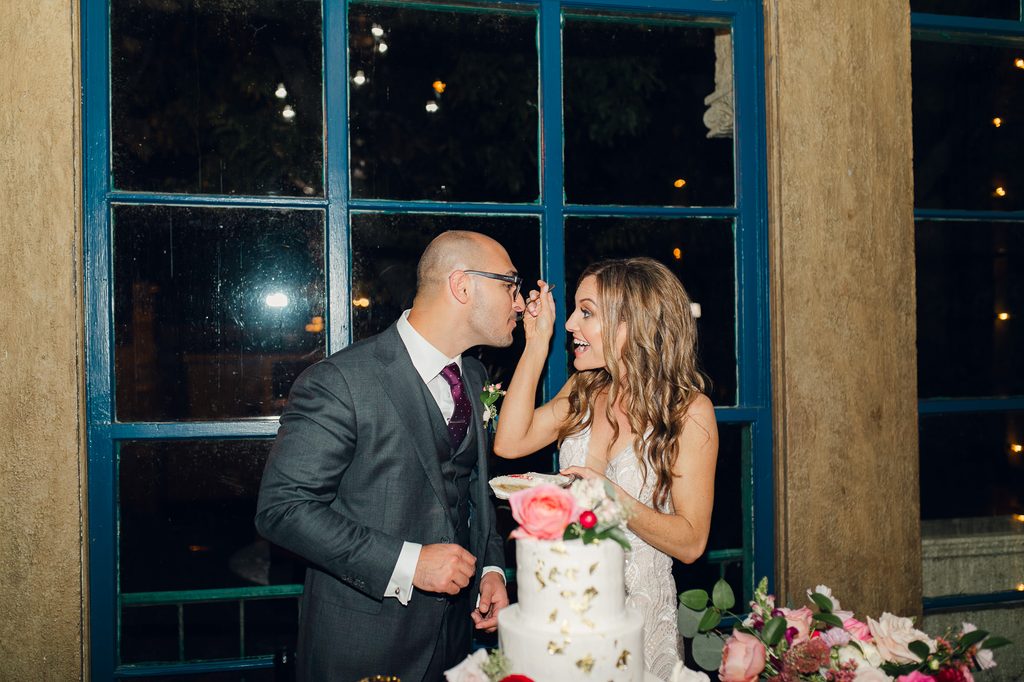 Megan feeding Keivan a bite of wedding cake beside the mansion’s blue-green windows. 